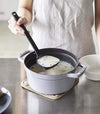 Front view of black Floating Ladle scooping soup out of pot by Yamazaki Home.