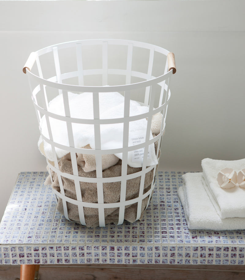 Front view of white Round Laundry Basket holding towels in laundry room by Yamazaki Home.