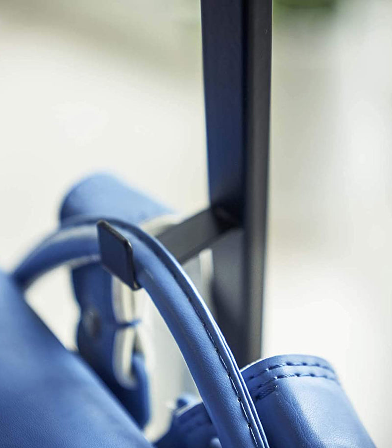 Close up view of black Rolling Coat Rack hook holding blue backpack by Yamazaki Home.
