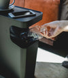 Close up view of black Side Table Trash Can holding phone and plastic bottle by Yamazaki Home.