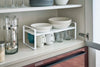 White Expandable Countertop Organizer expanded holding plates in kitchen cabinet by Yamazaki Home.