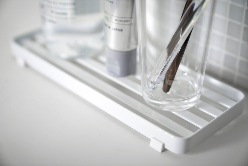 Close up view of white Slotted Tray holding sink accessories in bathroom by Yamazaki Home.