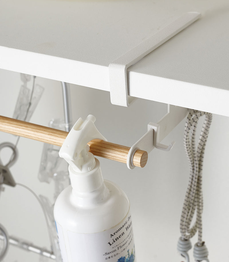 Close up of white Undershelf Hanger holding laundry supplies by Yamazaki Home.