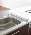 White Over the Sink Folding Drying Rack with folded or rolled up on kitchen counter.
