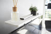 Close up view of white Compliant TV Shelf holding items behind TV by Yamazaki Home.