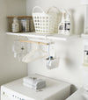 White Undershelf Hanger in laundry room holding laundry accessories by Yamazaki Home.