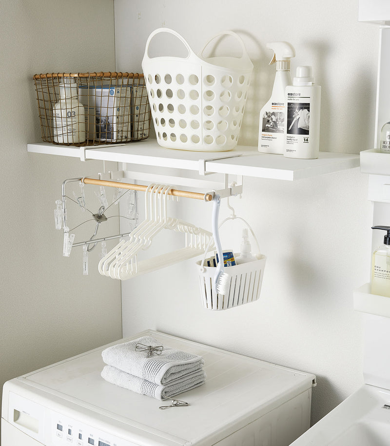White Undershelf Hanger in laundry room holding laundry accessories by Yamazaki Home.