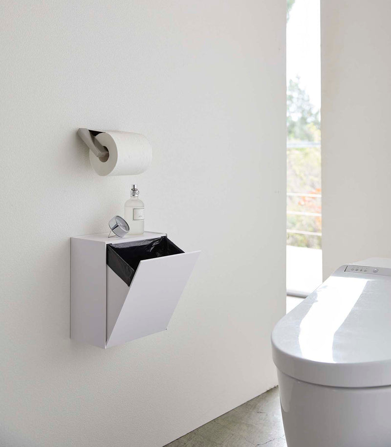 White Wall-Mount Storage open and holding trash bag on bathroom wall by Yamazaki Home.