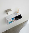 Aerial view of two open white Wall-Mount Storage bins holding items and trash bag in bathroom by Yamazaki Home.