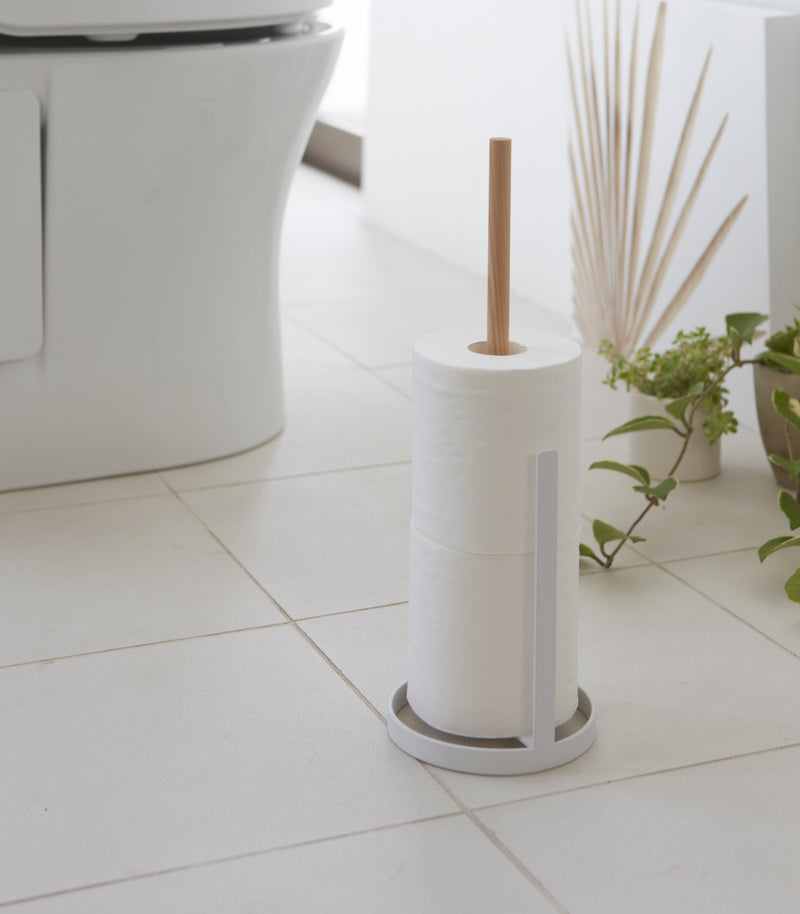 Side view of white Toilet Paper Stocker holding toilet paper in bathroom by Yamazaki Home.