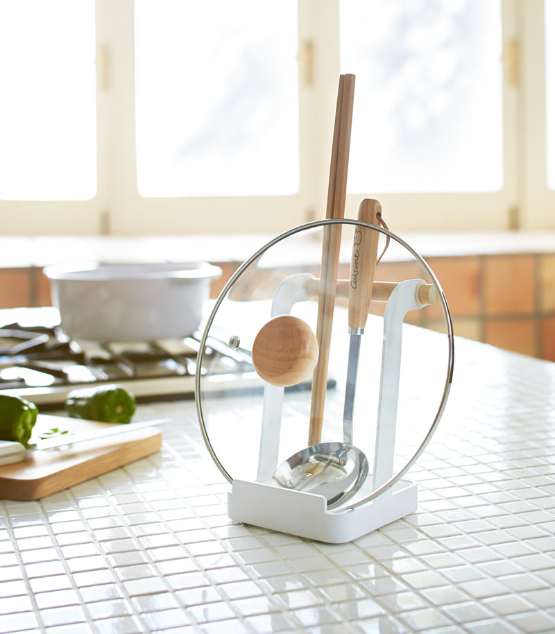 White Lid & Ladle Stand holding pot cover and kitchen utensils on kitchen countertop by Yamazaki Home.