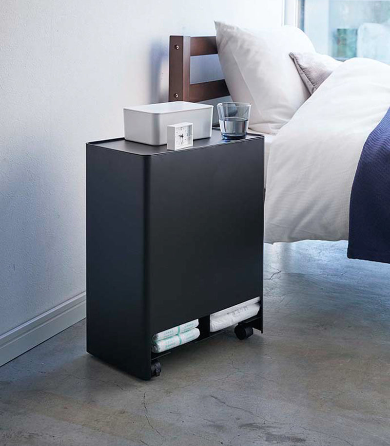 Black Rolling Diaper Stacker open containing diapers in bedroom by Yamazaki Home.