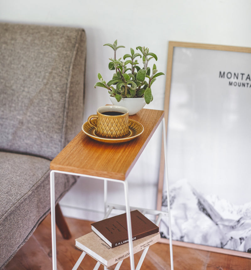 Side view of white End Table holding coffee cup, plant, and books by Yamazaki Home.