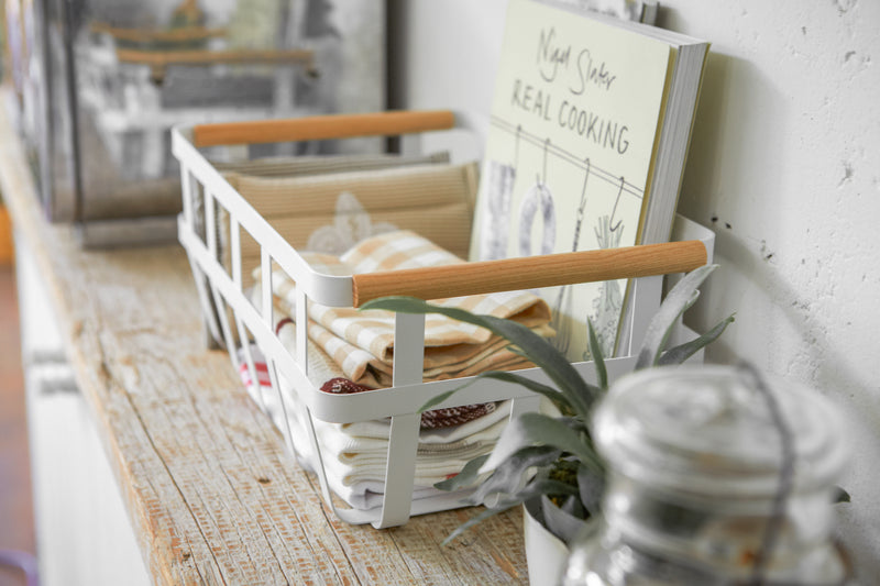 Side view of white Storage Basket holding book and cloth napkins on shelf by Yamazaki Home.